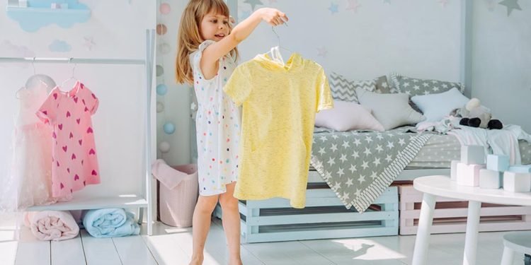 Beautiful little girl choosing a dress in the kids room